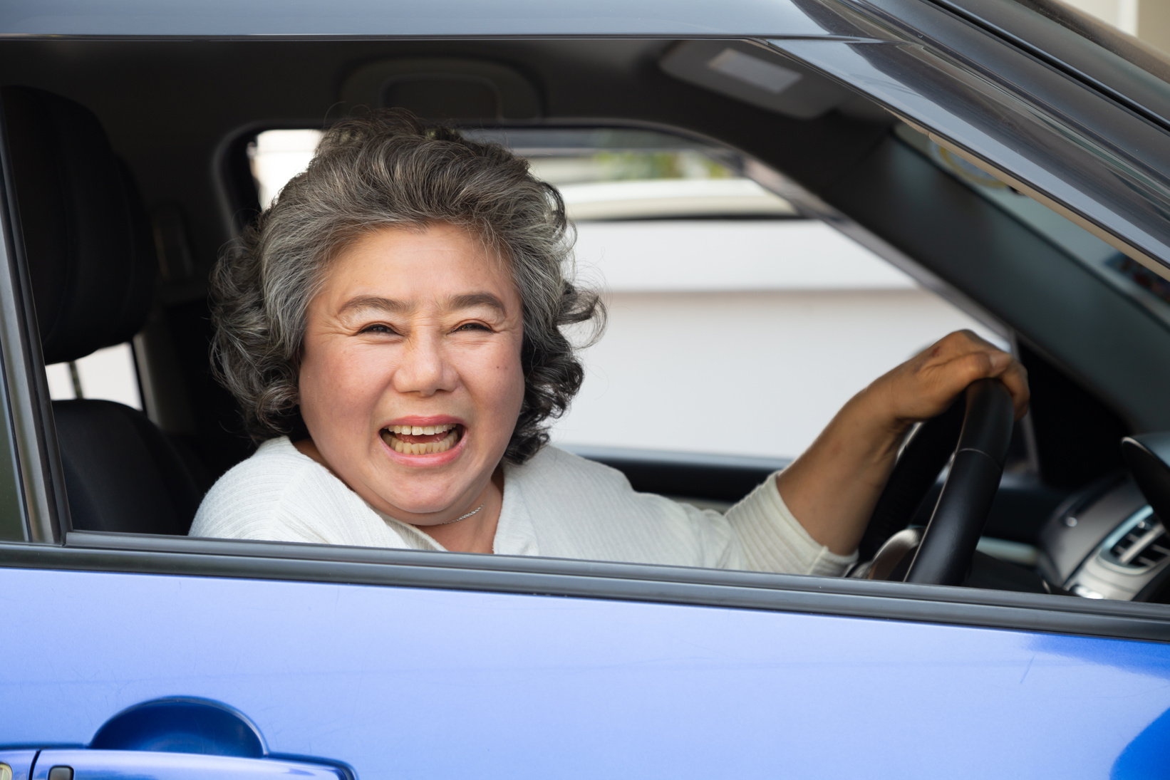 Asian senior woman driving a car and smile happily with glad positive expression during the drive to travel journey, People enjoy laughing transport and drive thru concept