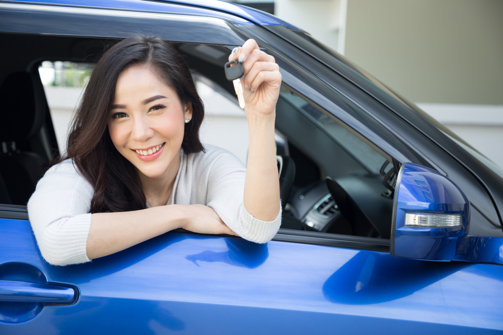 Young happy Asian car driver woman smiling and showing new car keys. Novice drivers concept